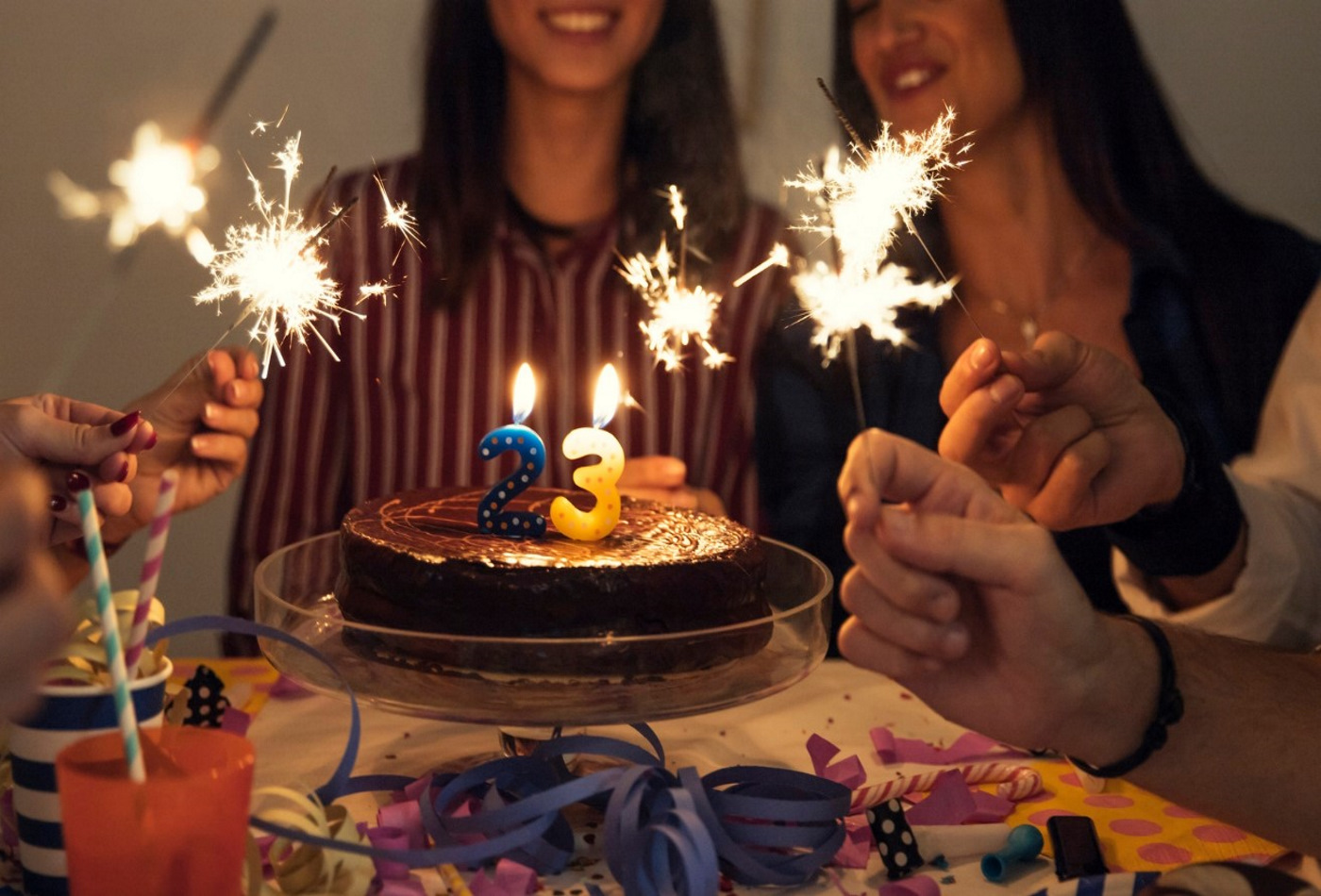 Várias pessoas a celebrar um aniversário, com um bolo no centro e com várias velas acesas.